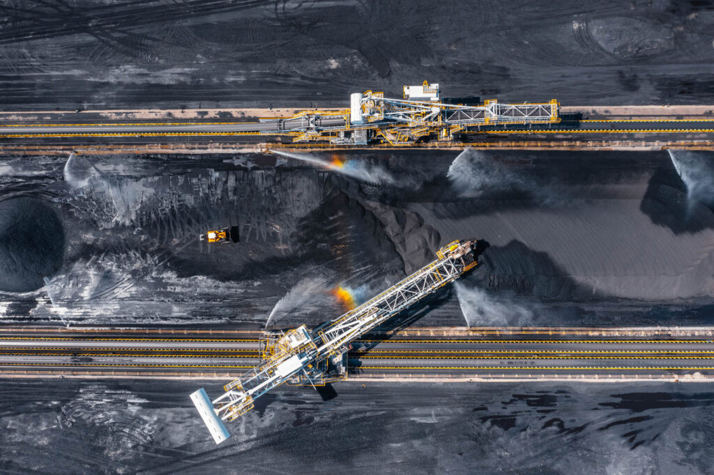 Aerial view of large coal stockyard with heavy machinery moving coal at a terminal for global shipment.