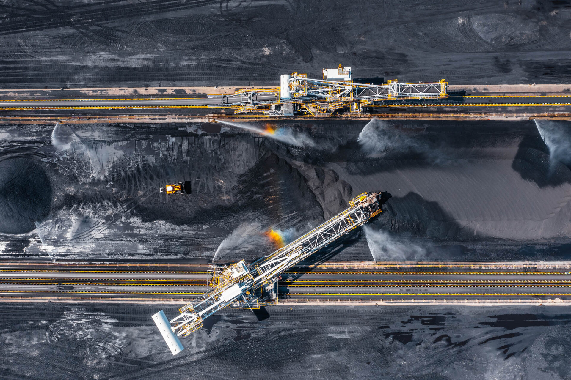 Aerial view of large coal stockyard with heavy machinery moving coal at a terminal for global shipment.