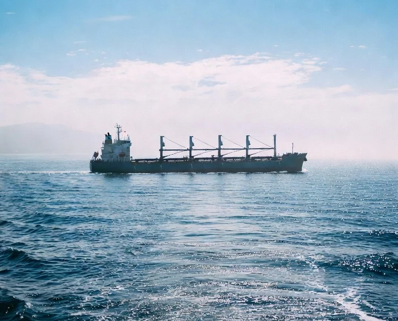 Bulk cargo ship sailing across the sea under a clear blue sky.
