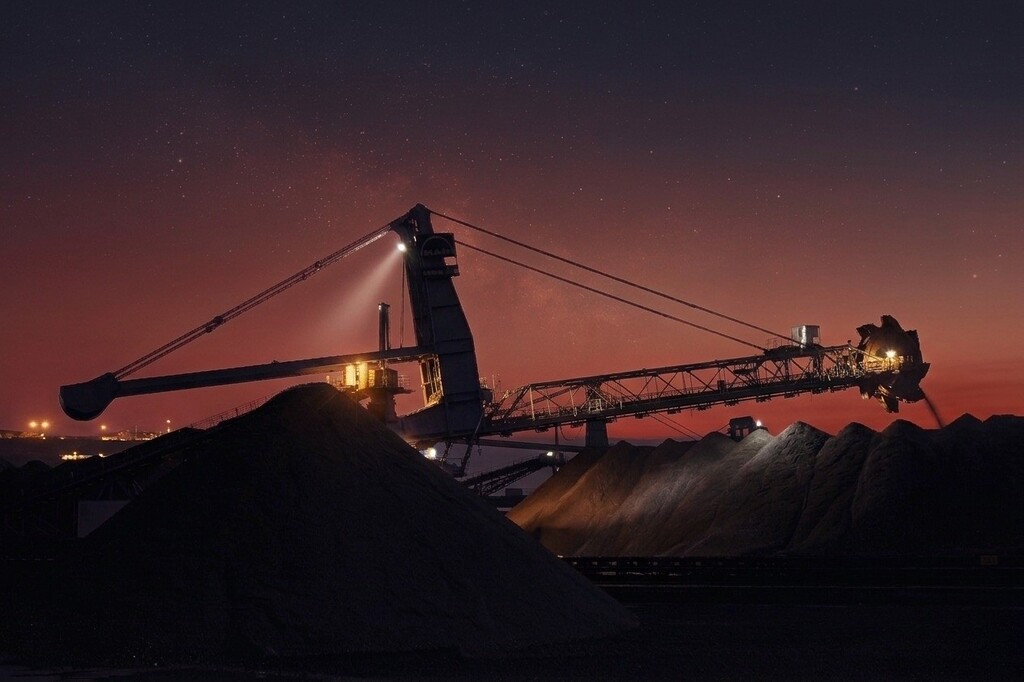 Coal stockpiles and loading equipment at a coal terminal during nighttime operations amid changing global coal prices
