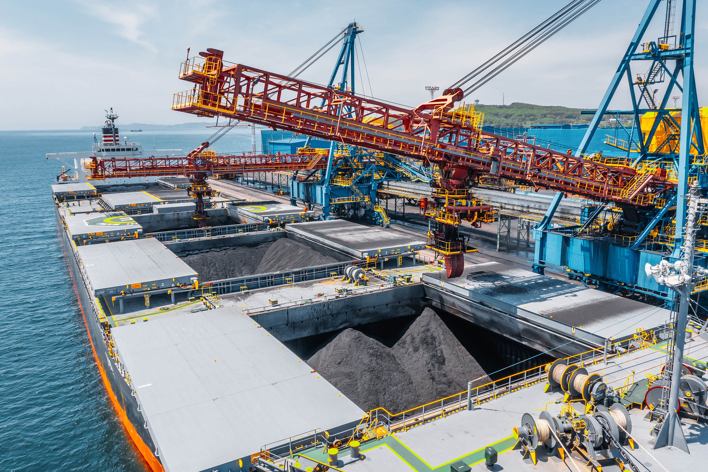 Coal being loaded onto a cargo vessel at a port terminal using conveyor equipment.
