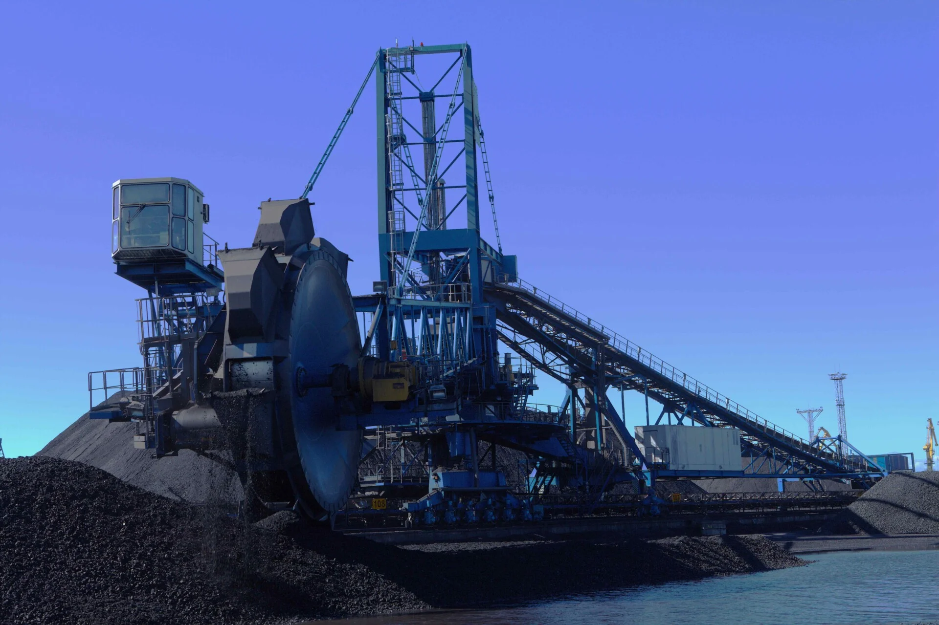 Coal handling machine loading and moving coal at an industrial coal terminal.