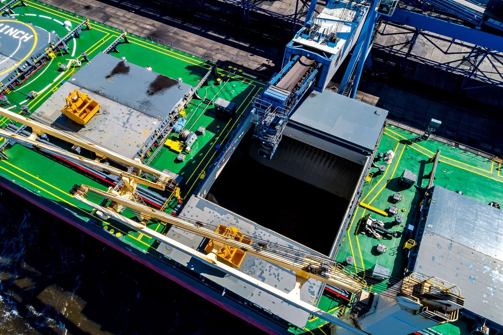 Aerial view of coal being loaded into a bulk carrier at a port terminal.