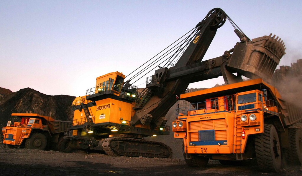 Large excavator loading coal into haul trucks at an open-pit coal mine in Kuzbass.