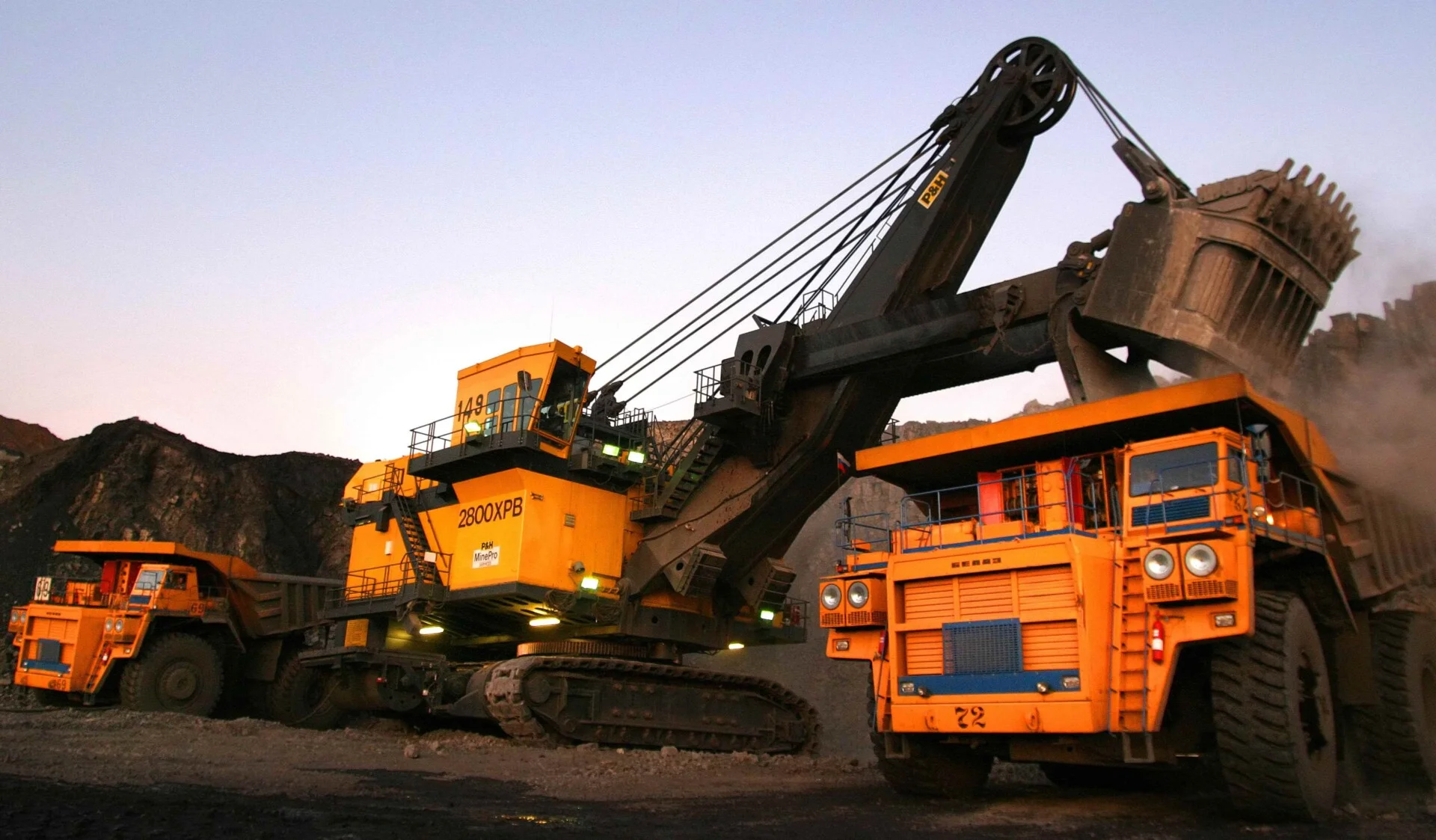 Large excavator loading coal into haul trucks at an open-pit coal mine in Kuzbass.