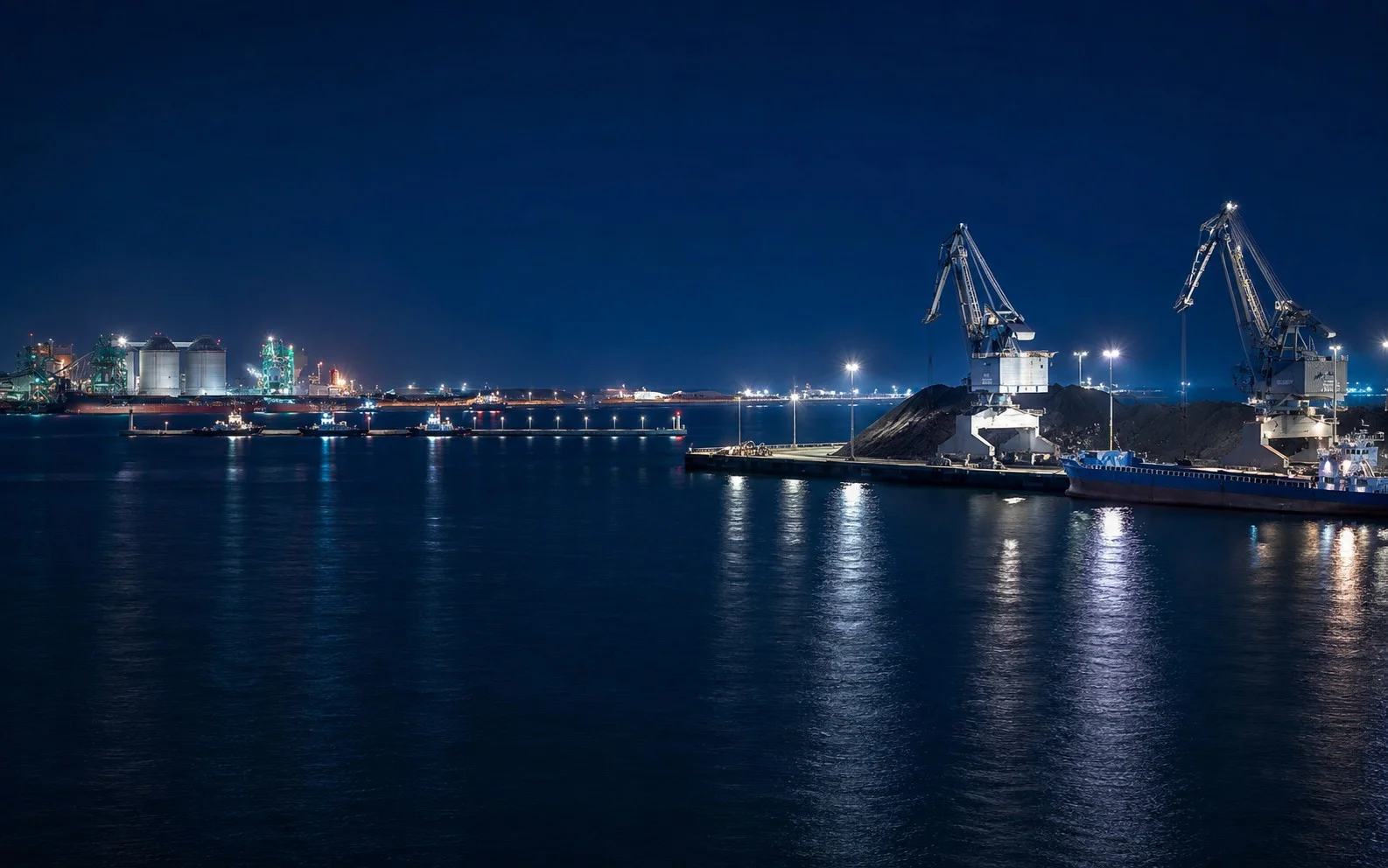 Night view of a coal terminal with cranes, stockpiles and ships at a South Korean port.