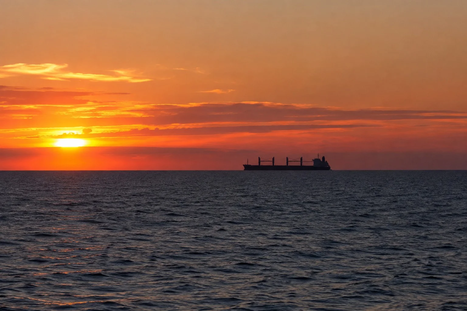 Bulk carrier sailing across the sea at sunset under an orange sky.
