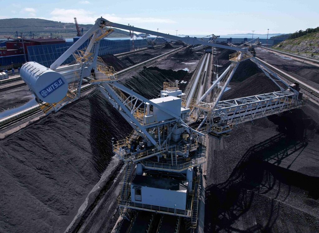 Large coal handling machine working beside coal stockpiles at an export terminal.
