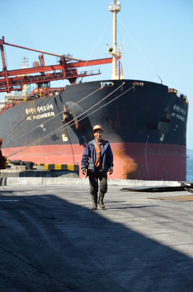 Port worker walking in front of a bulk carrier during coal handling operations at a Chinese port.