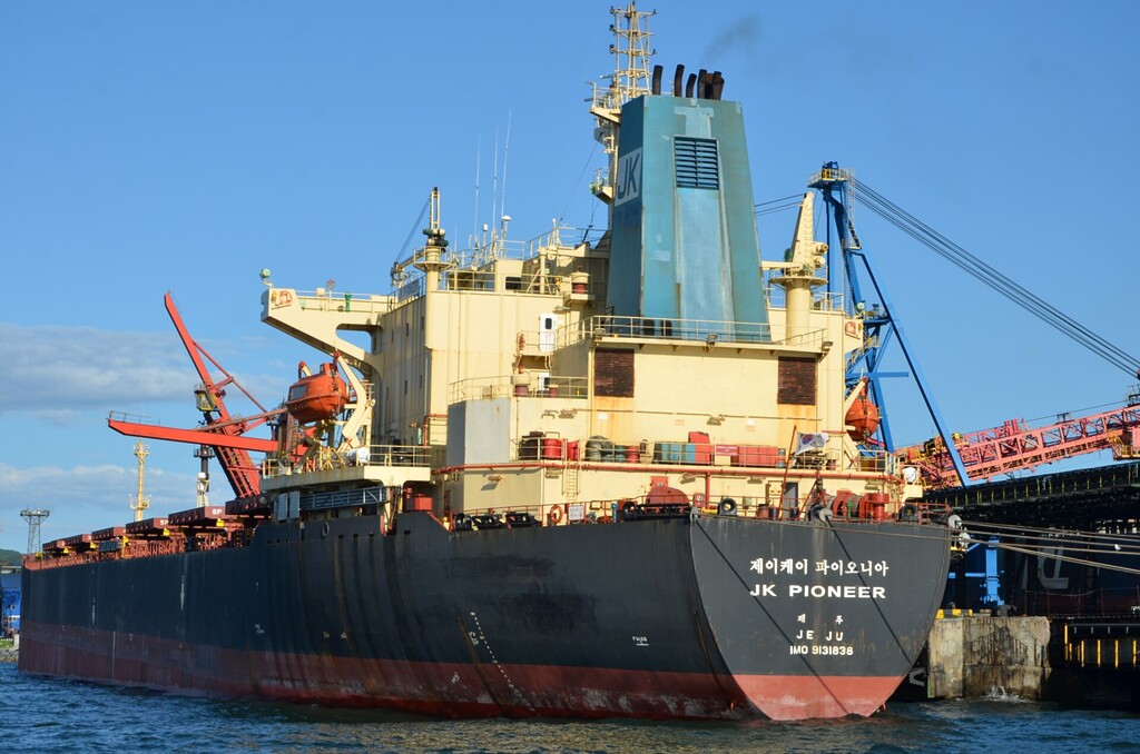 Bulk carrier docked at a South Korean coal terminal with loading equipment alongside.