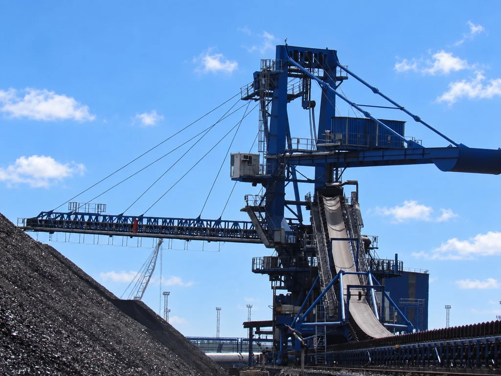 Large coal handling and conveyor equipment operating beside a coal stockpile at an export terminal.