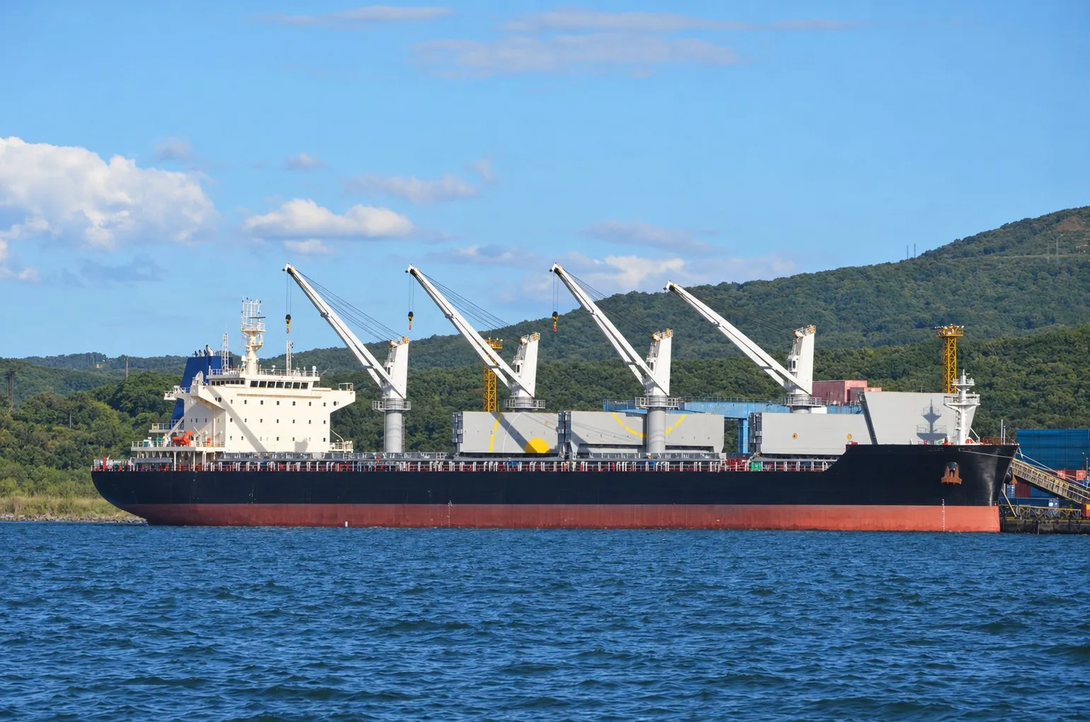 Large bulk carrier docked at a coal terminal with shipboard cranes and loading infrastructure.